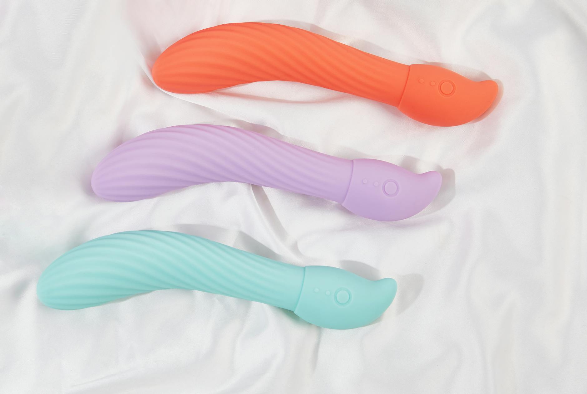 Three colorful silicone vibrators arranged on white fabric, showing smooth texture designed for sensitive skin