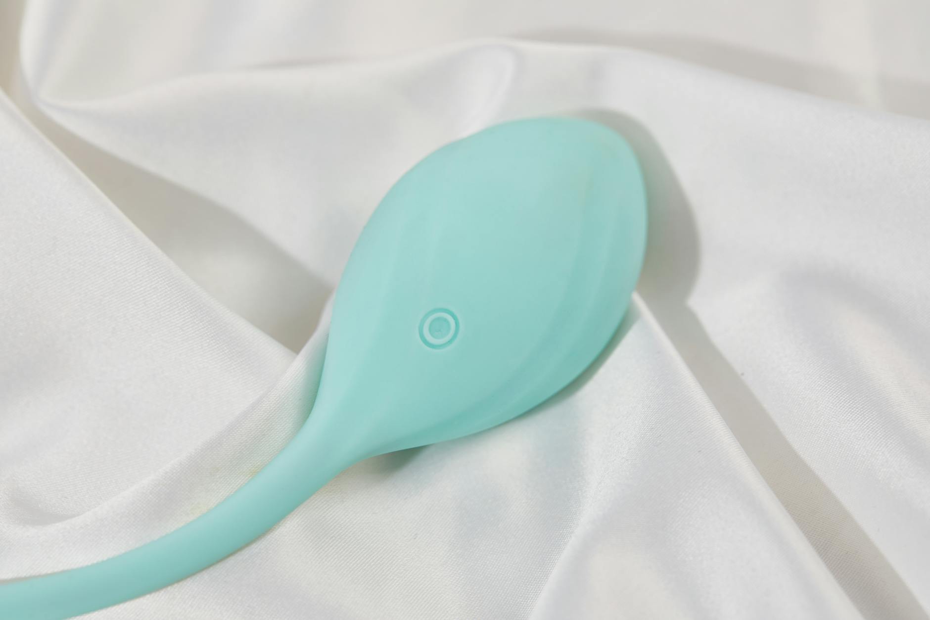 A smooth teal clitoral vibrator resting on white silk, charged and ready to use