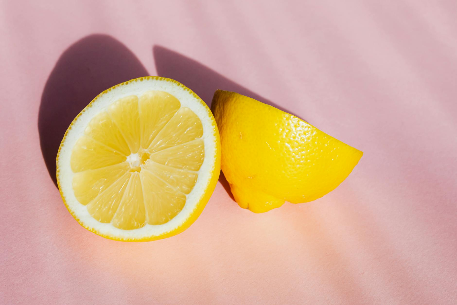 Fresh lemon halves on pink background in sunlight, symbolizing renewed sensation and vitality