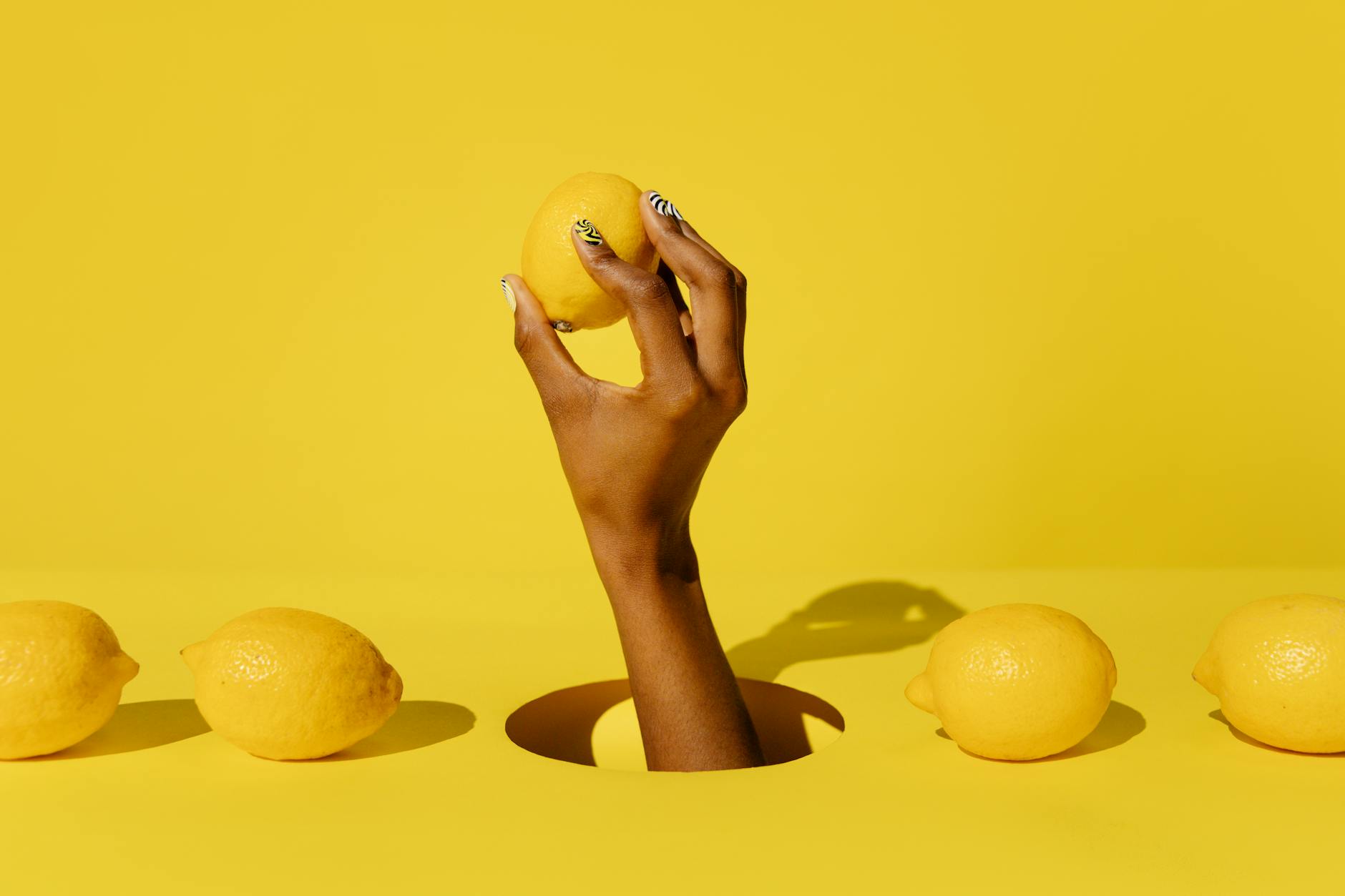 A creative composition featuring a hand holding a lemon against a vivid yellow background, conveying a fresh and citrusy vibe