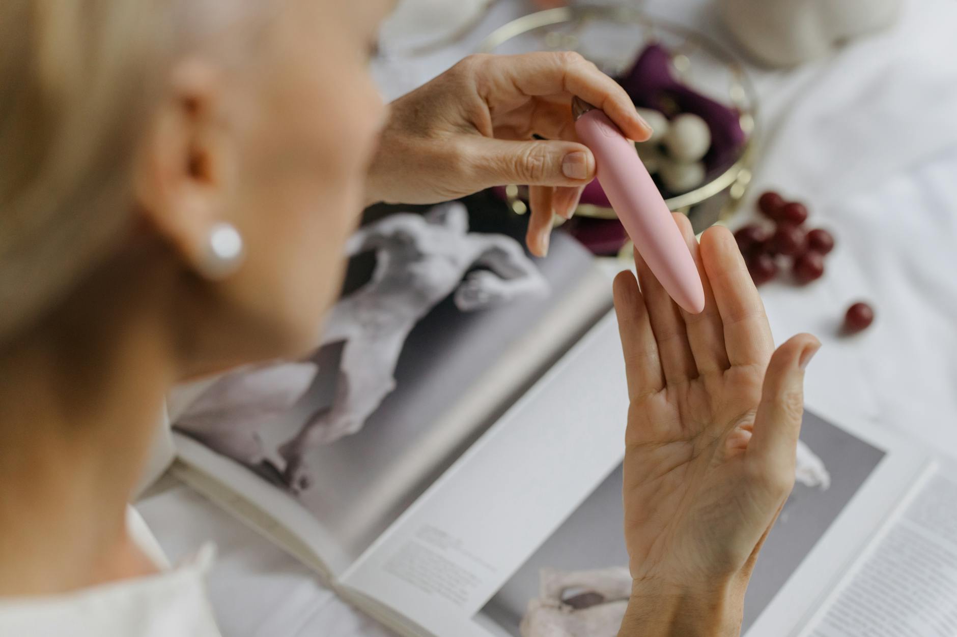 Woman holding a pink vibrator with art books in background, representing intimate exploration and pleasure