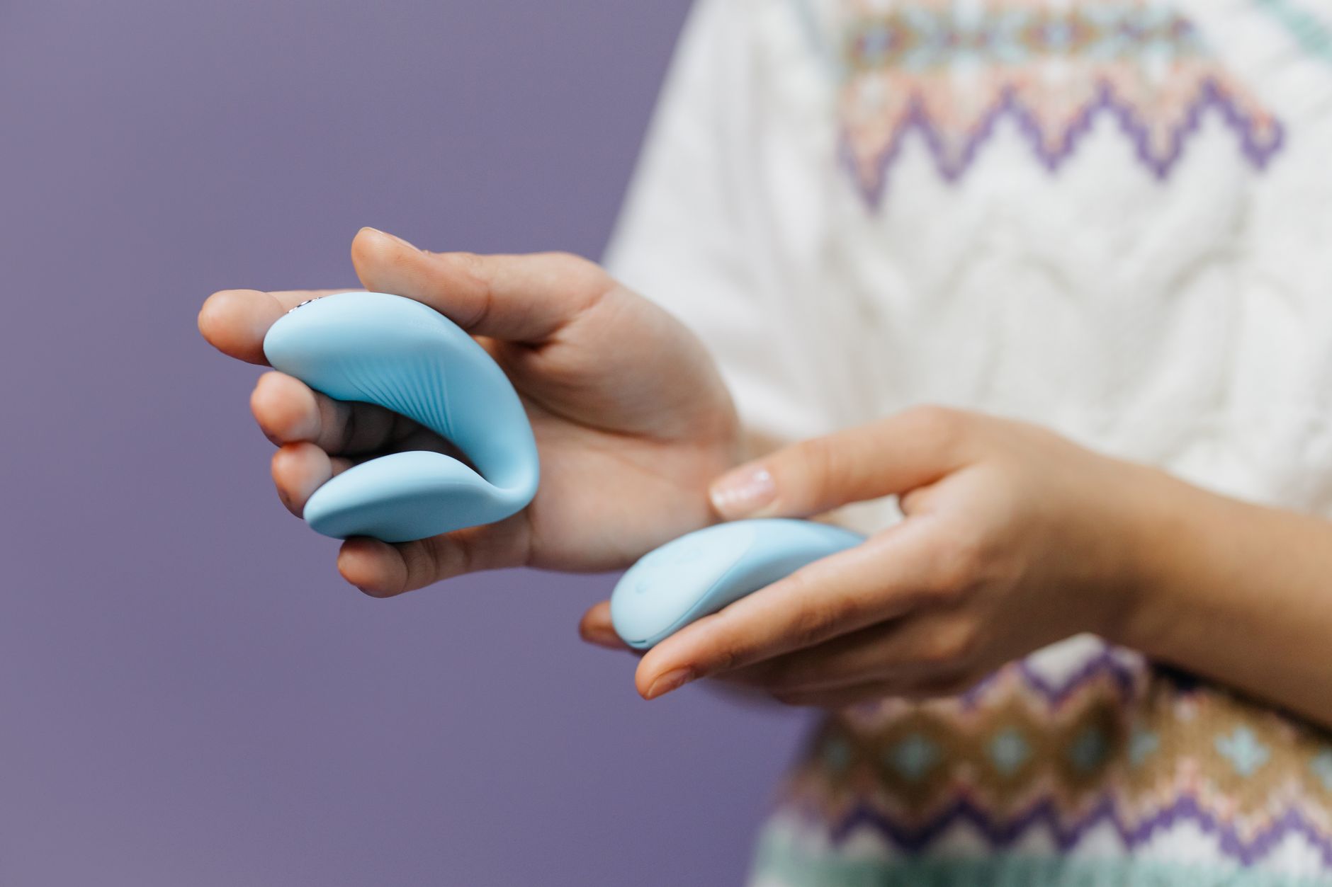 Two hands holding colorful vibrators against a pastel background.