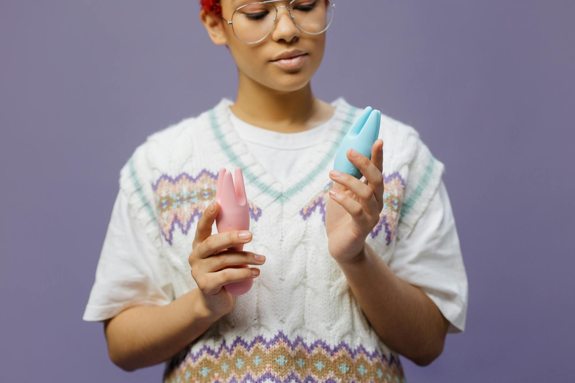 Woman holding blue and pink silicone vibrators in a thoughtful, contemplative moment