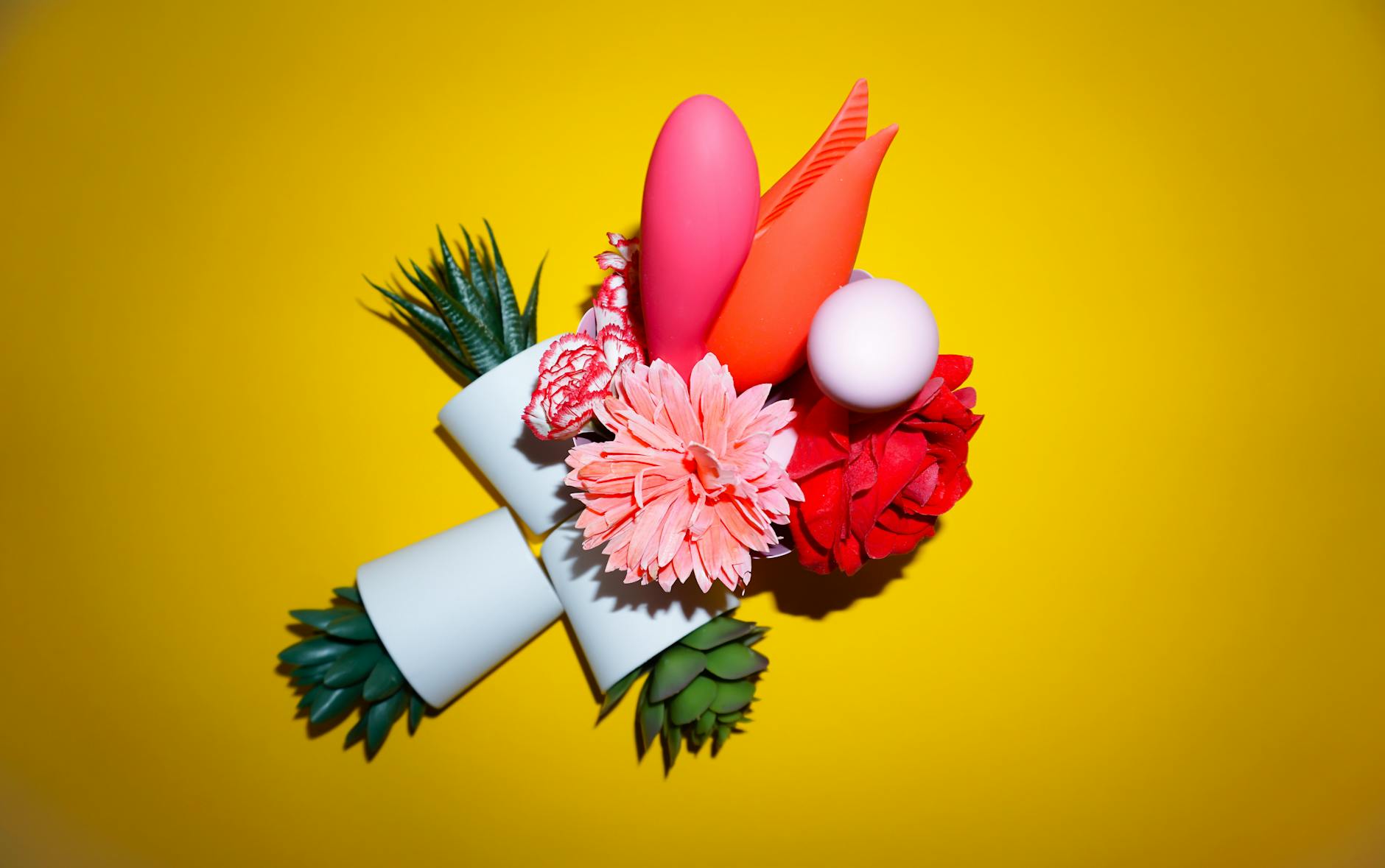 Colorful arrangement of flowers and abstract objects on a bright yellow background, representing wellness and pleasure.