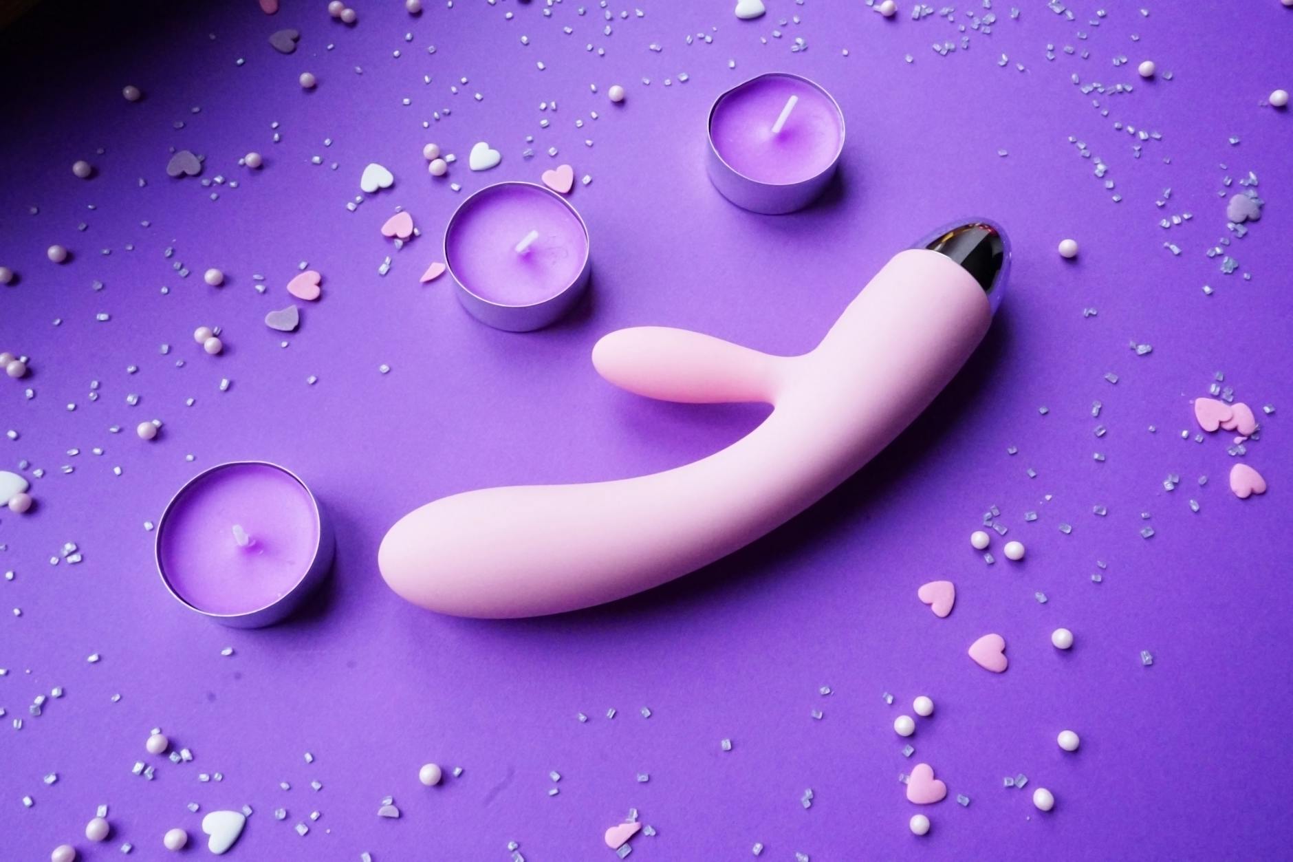 Pink vibrator on a purple background with heart confetti and candles for romantic reconnection