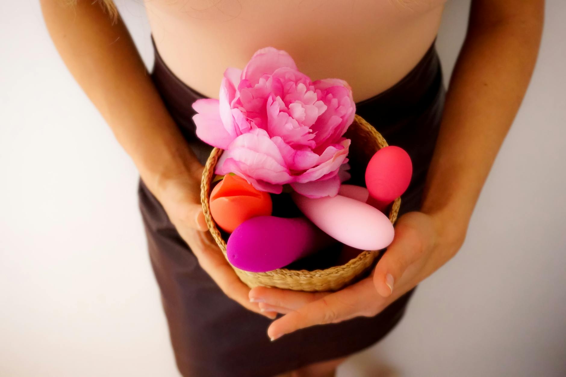 Colorful vibrators and toys displayed in a woven basket with pink flowers